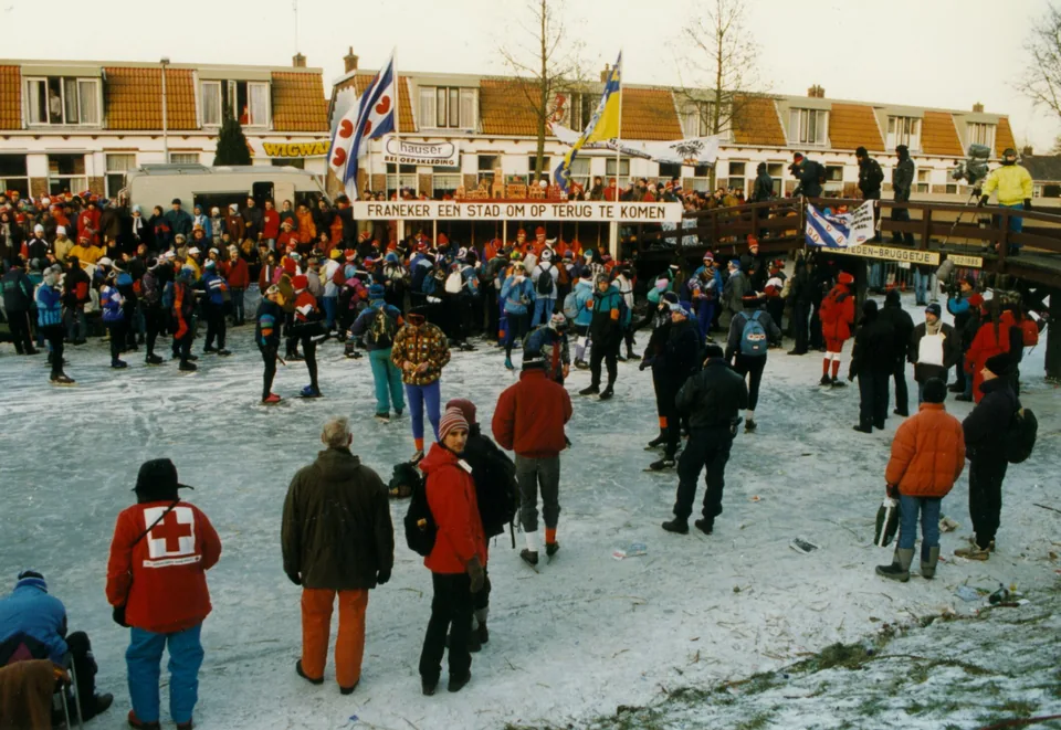 Schaatsers rijden langs een grote groep toeschouwers en spandoeken in Franeker.