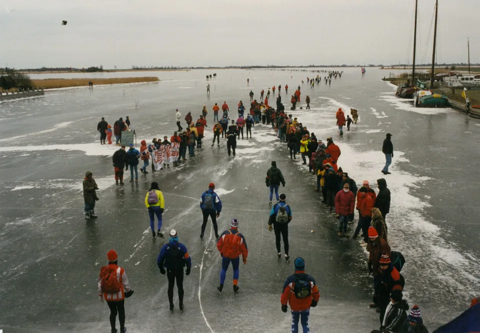 Toerrijders in gekleurde winterkleding komen over het ijs bij Galamadammen.