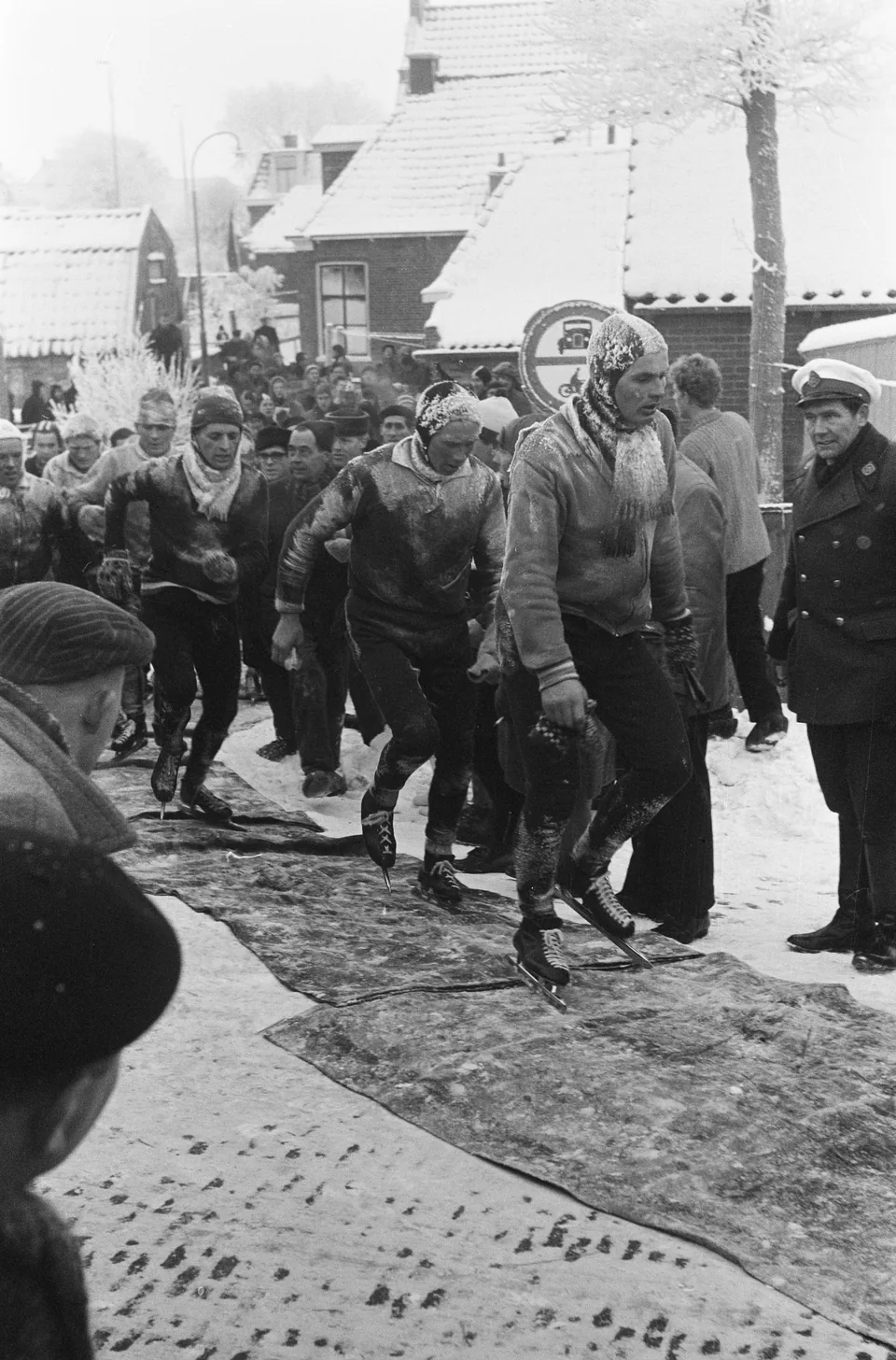 De kopgroep loopt op schaatsen over matten door het besneeuwde Hindeloopen.