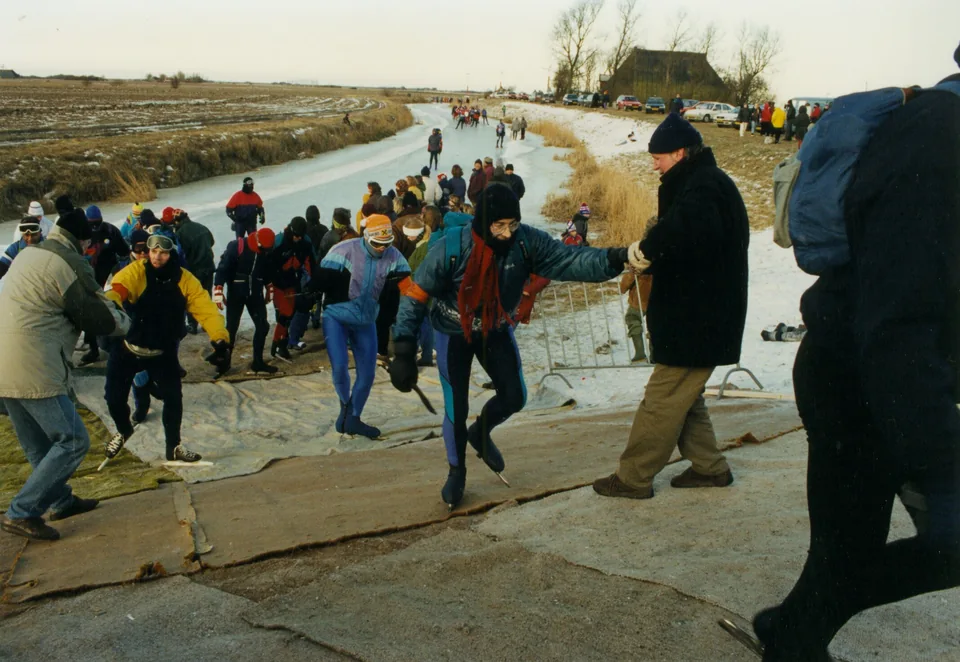 Schaatsers lopen met hun schaatsen aan over een met matten bedekte kluunplaats bij Franeker.